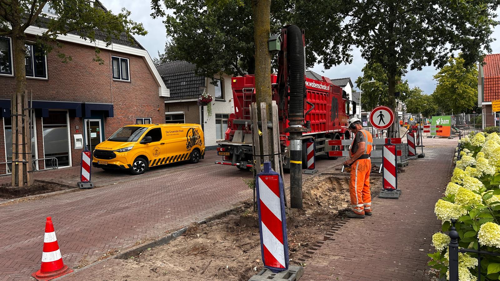 Bedrijfsauto van De Groenste Stad bij graafwerk met een zuigwagen langs bestaande straatbomen